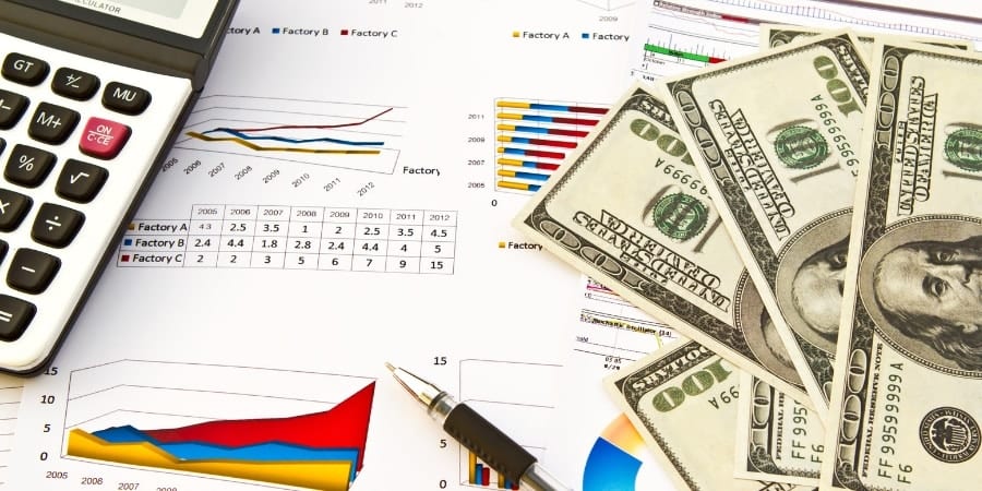 Foto de calculadora, caneta, notas de dólares e gráficos para representar o trabalho de uma assessoria cambial